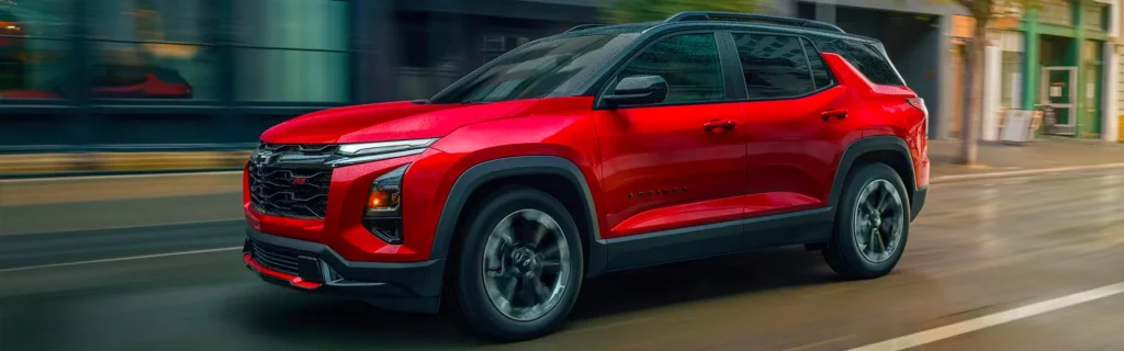 The image shows a 2026 Chevrolet Equinox in a striking red color, cruising down an urban street. The SUV’s dynamic design is highlighted by its aggressive front grille and sleek, sporty profile.