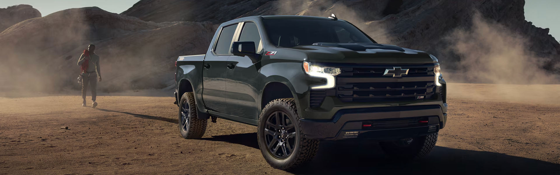 2026 Chevy Silverado crew cab truck with Z71 off-road package, black wheels, and lifted suspension, driving through dusty desert setting