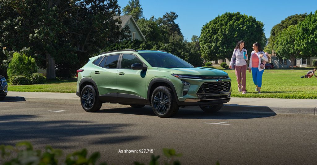 A sleek 2026 Chevrolet Trax in Cacti Green parked in front of a modern glass building.