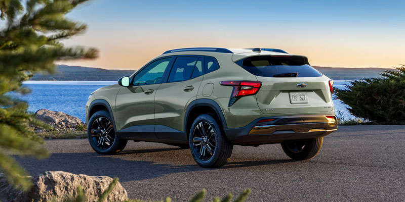 A green Trax is parked on a coastal road at sunset, overlooking a calm blue sea. The ambiance is serene and the car's sleek design is highlighted.
