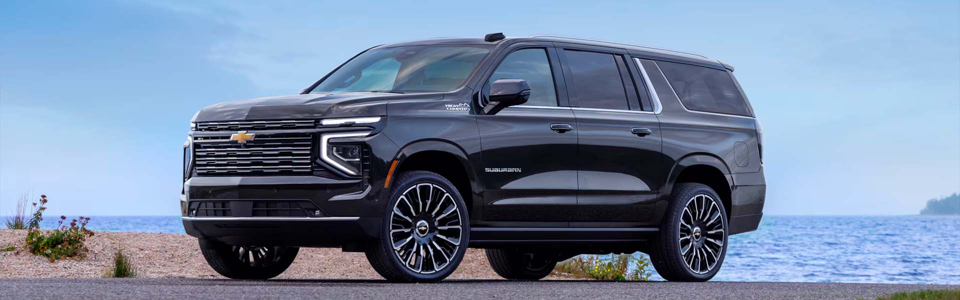 2026 Chevrolet Suburban parked near a beach, showcasing its sleek black exterior and shiny wheels.